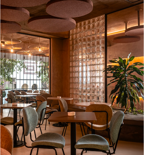 Cafe interior with textured circular pendant lights, metal slat partition, and lush potted plants