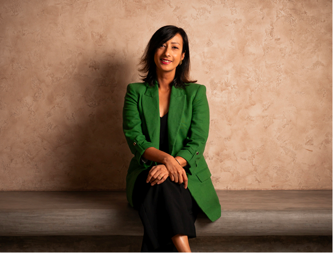 Founder portrait seated on a stone ledge, wearing a green blazer