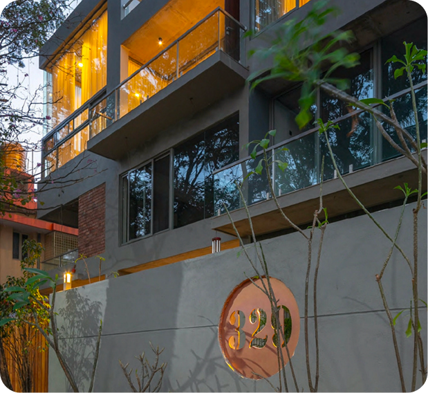 Modern multi-storey building at dusk with concrete facade, glass balconies, and illuminated circular house number