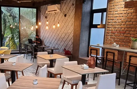 Industrial cafe with brick wall, white chairs, wood tables, and Edison pendant lights