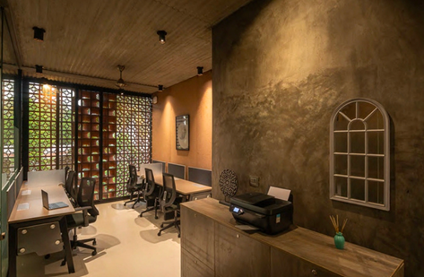 Workspace with concrete wall, terracotta accent, wood desks, and geometric screen