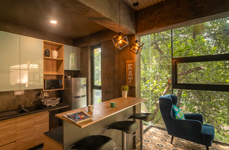 Compact kitchen and breakfast bar with wood counter, stools, and large window to trees