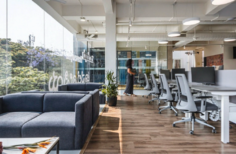 Bright open office with lounge sofa, white desks, and floor-to-ceiling windows